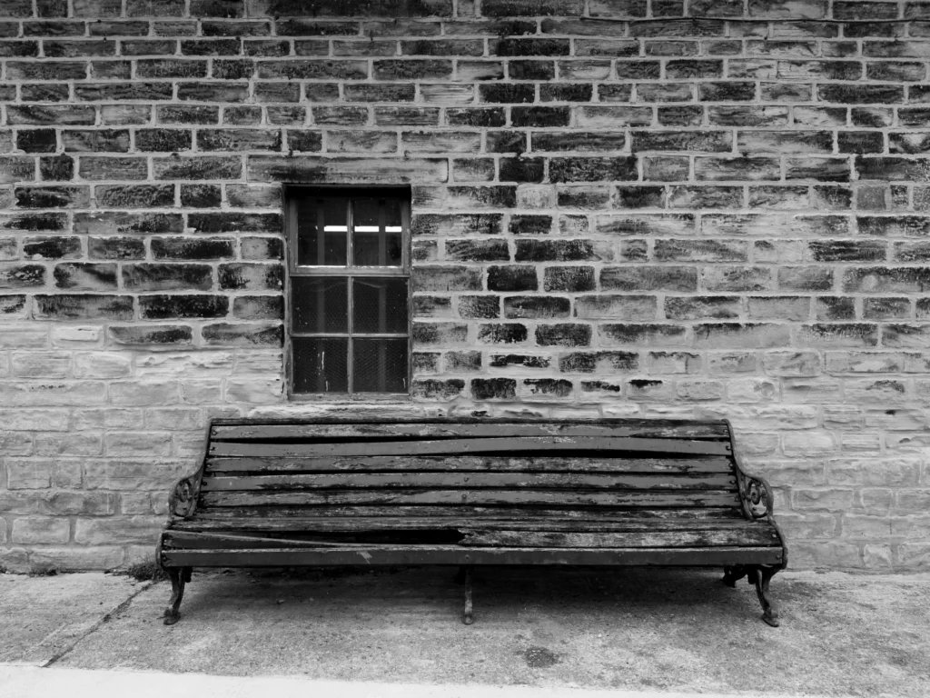 An old Victorian bench in front of a wall with a single window.