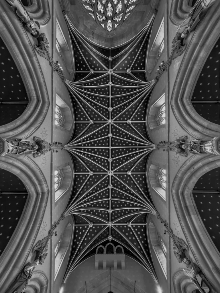 A black-and-white photo looking directly up at a symmetrical cathedral ceiling with neo-Gothic architecture.