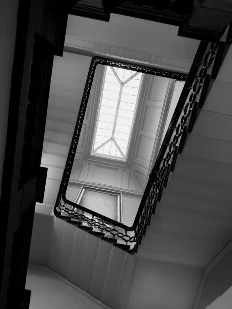 Looking up towards a ceiling window from the bottom of a spiral staircase.