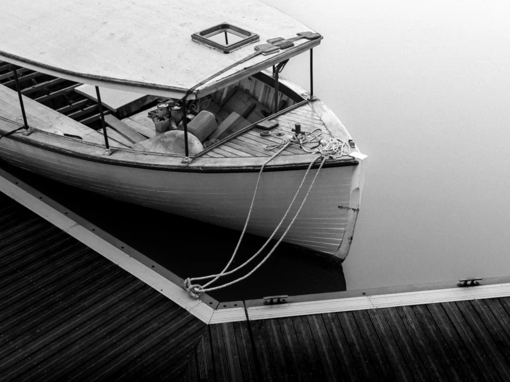 A black and white photo a boat being renovated on perfectly still water.