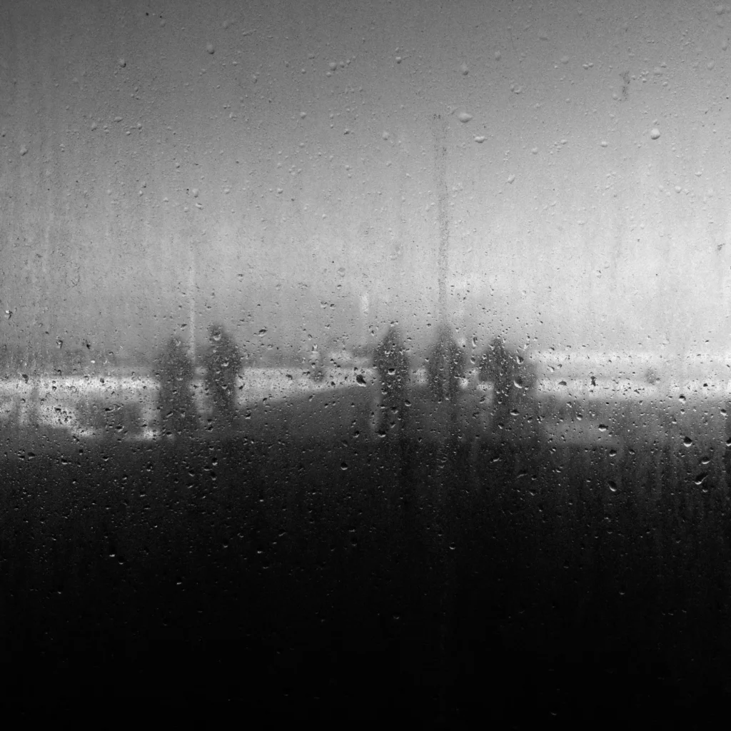 A black and white photo of people on a ferrt deck shot through a rainy window.