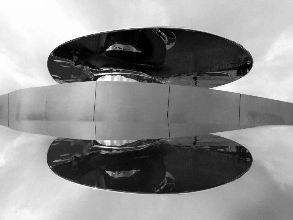 A black and white photo of an abstract architecture structure feflected in a surface in front of it.